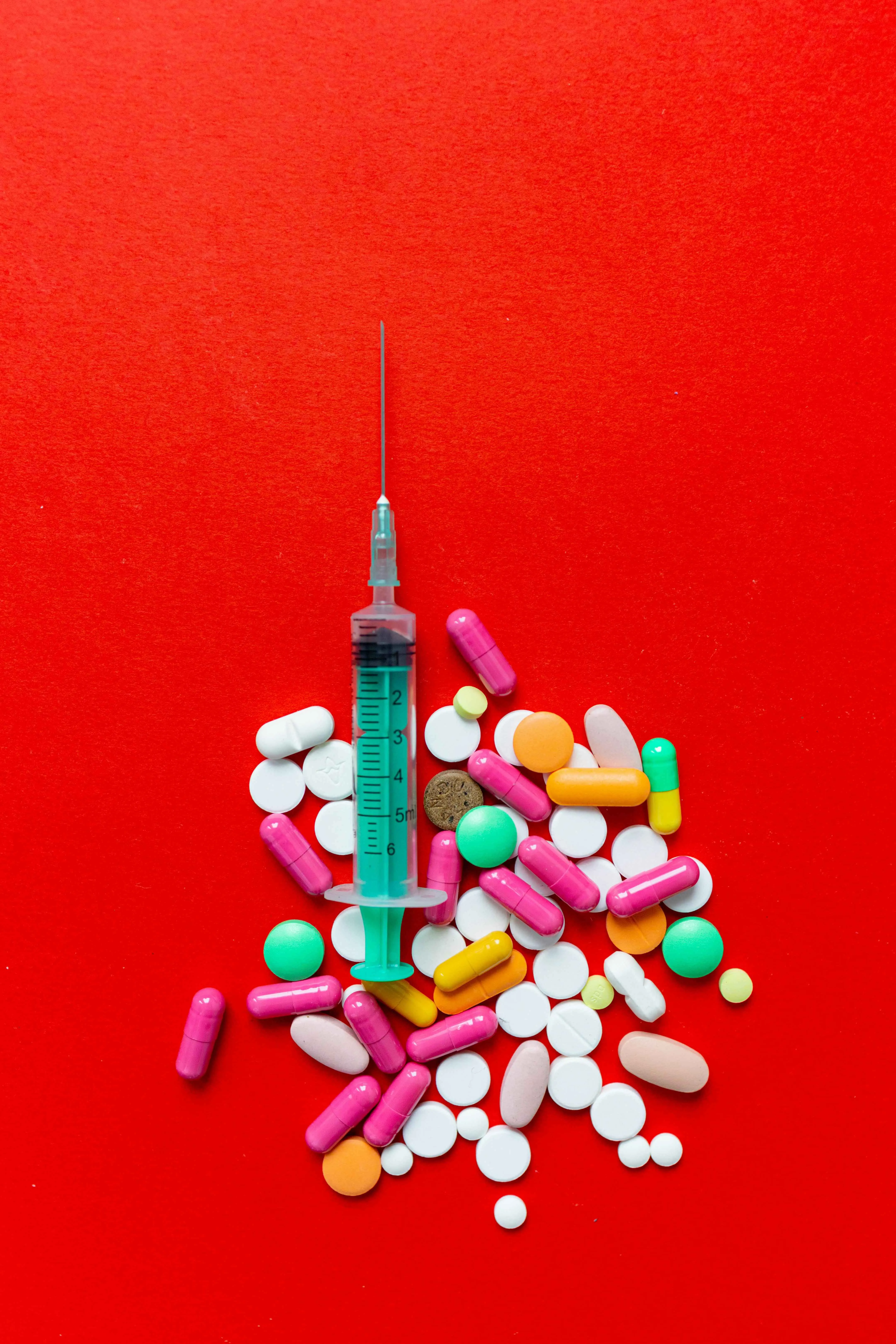 Pills and an injection placed against a red backdrop