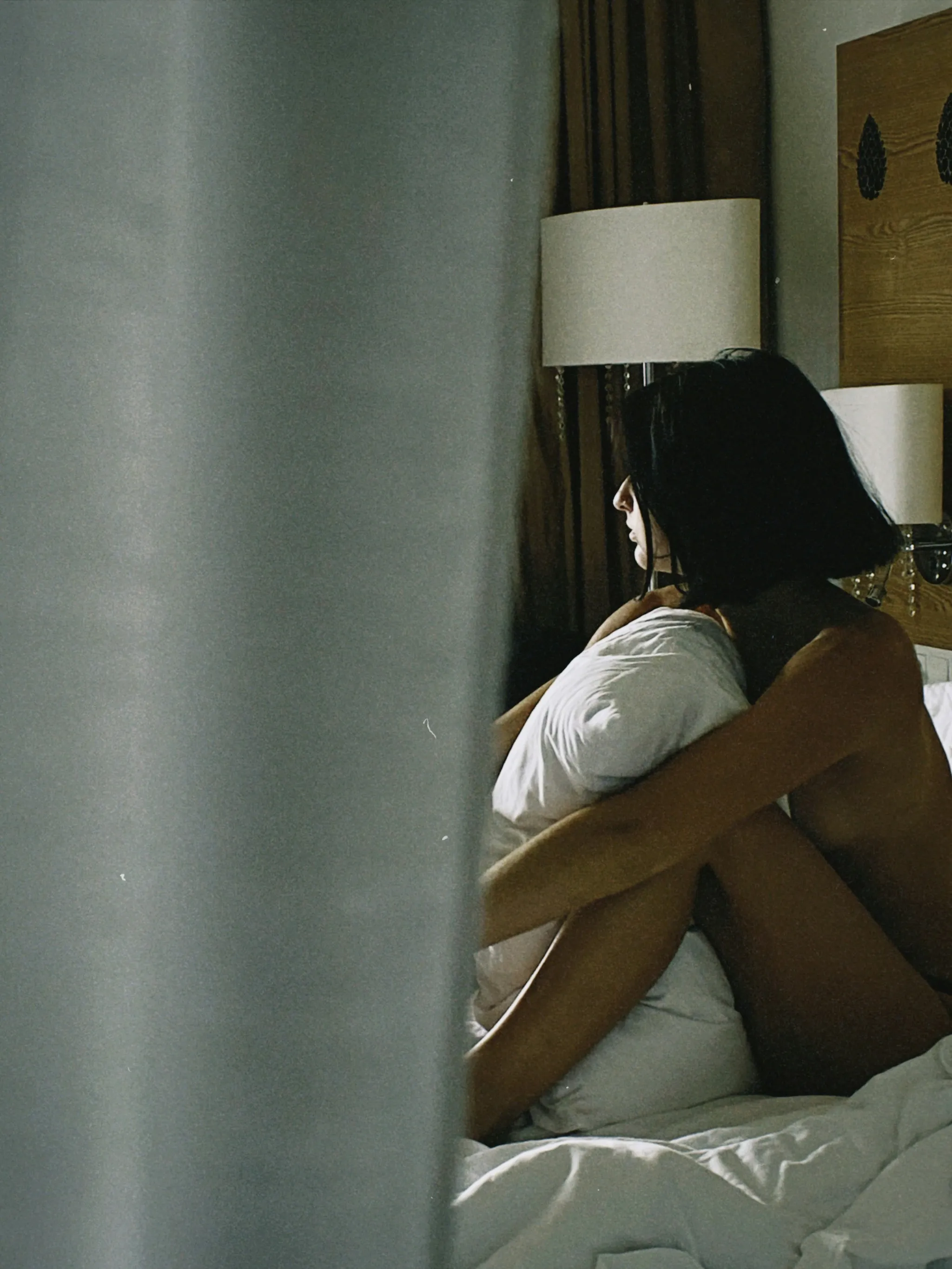 A woman sitting sadly on her bed with white linen