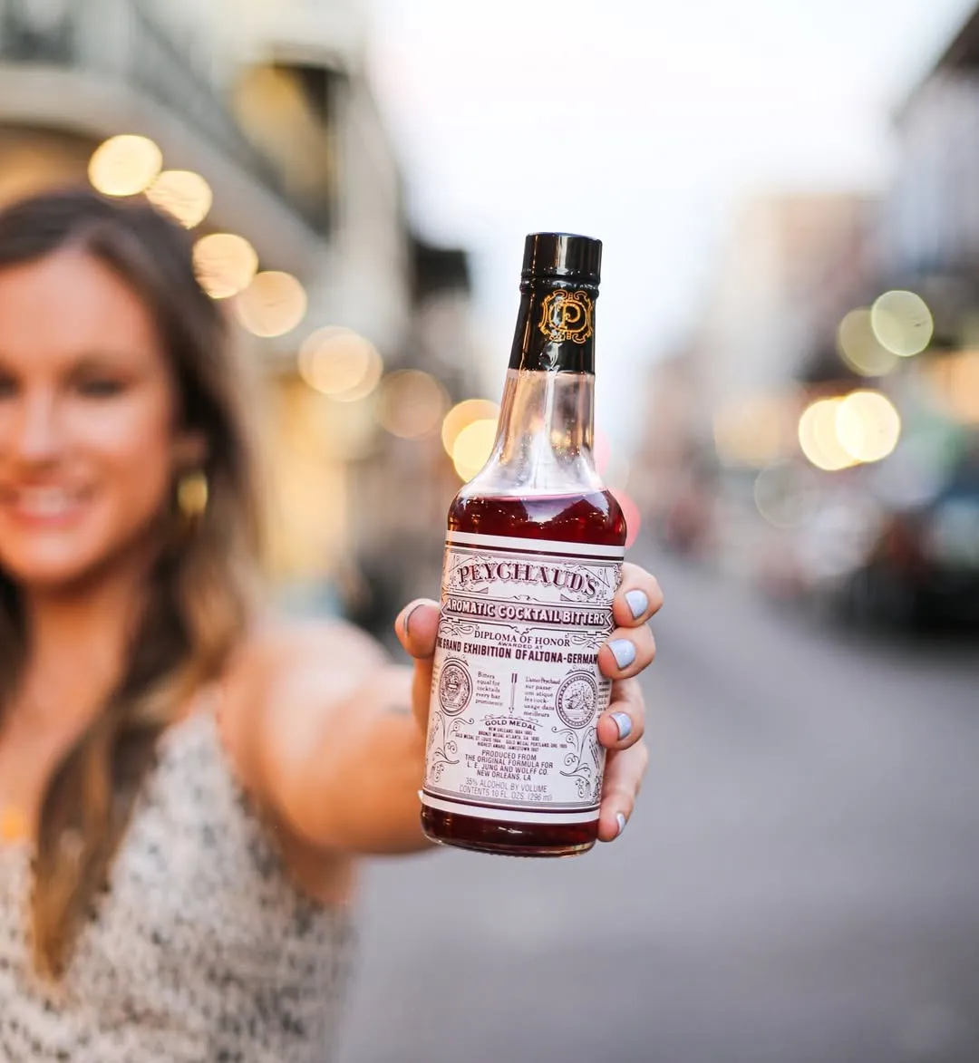 A woman holds a bottle of Peychaud's Bitters to show how cocktail bitters in India are getting popular in India with Indian cocktail culture embracing luxury cocktail ingredients including non alcoholic bitters India