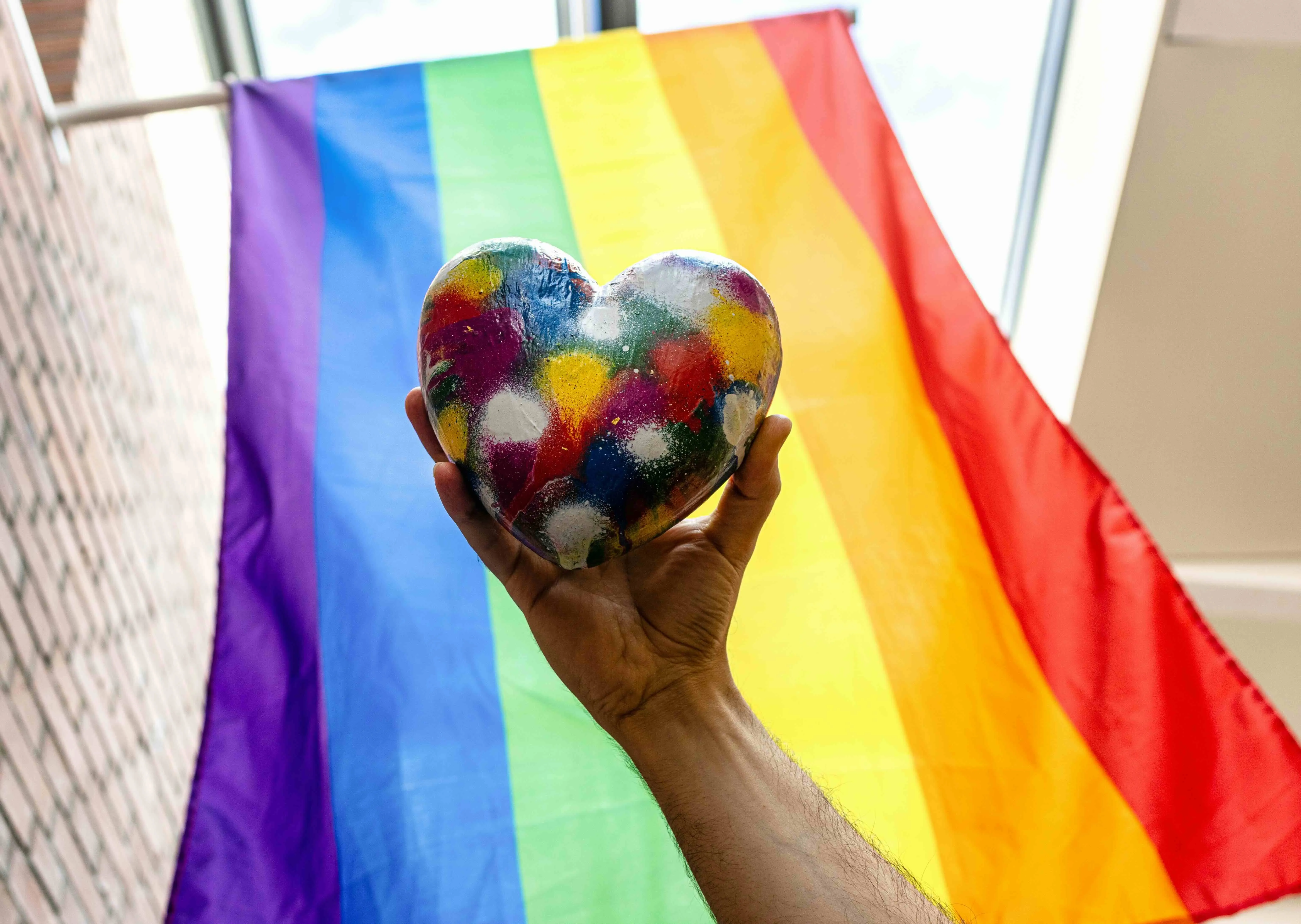 A picture of a person holding a multicoloured heart against a pride flag to show the inclusivity of discovering sexuality as an adult in a country like India where societal norms lead to queer late bloomers and late-life queerness India