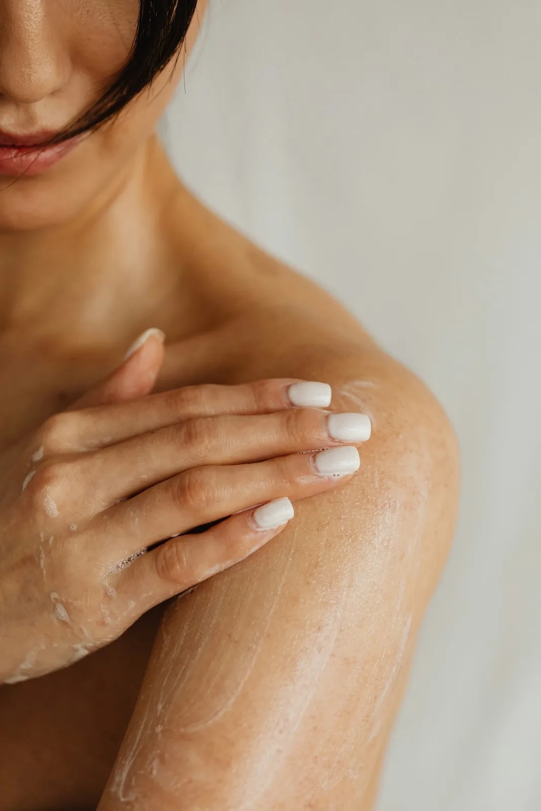 A woman applying a skincare product on her shoulders