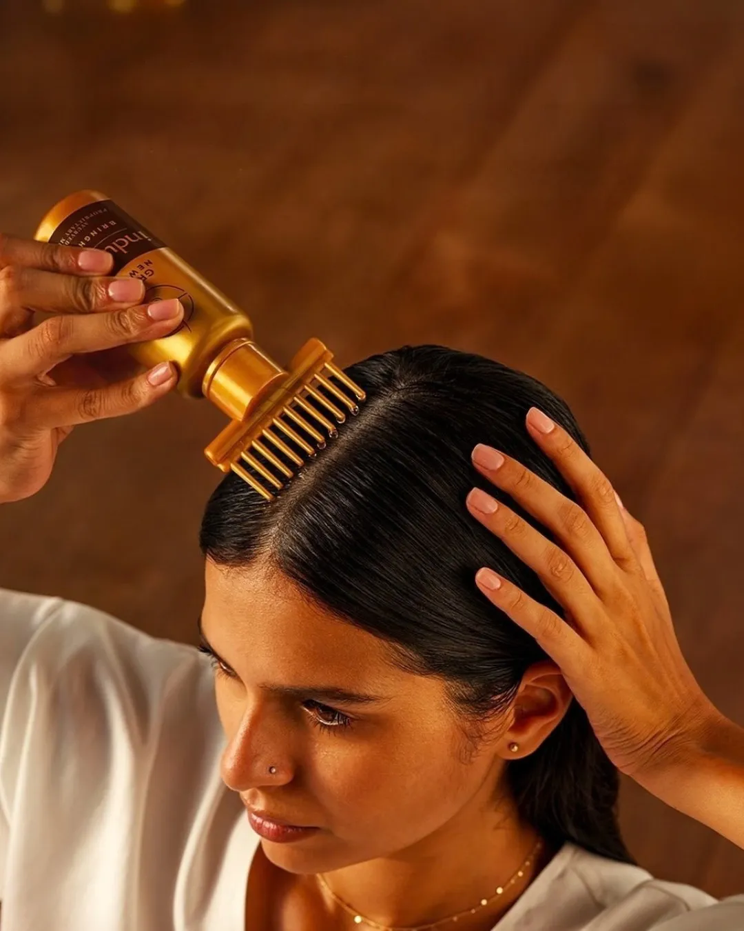 A bottle of indulekha hair oil in a woman's hand being applied on the head