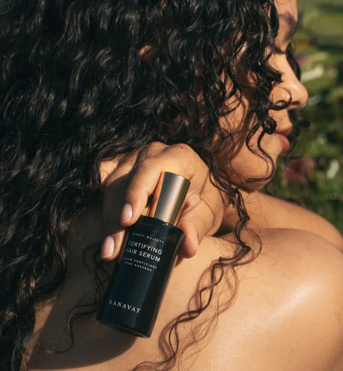 A backshot of a woman with curly hair holding a bottle of the best hair oil