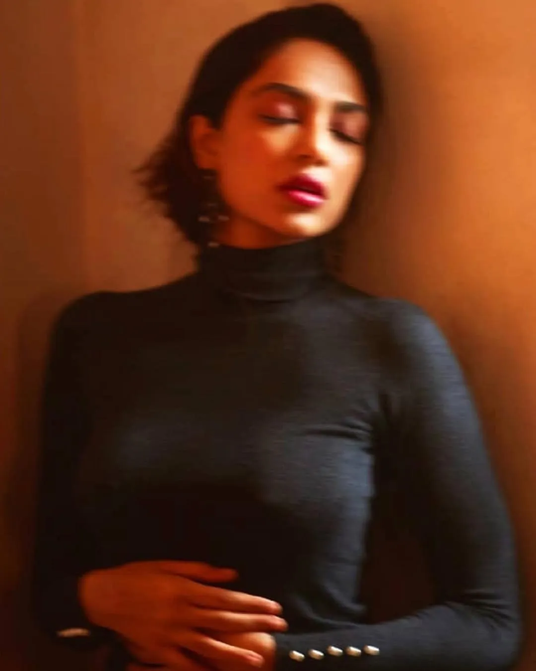 A blurry image of Sobhita Dhulipala in a black top