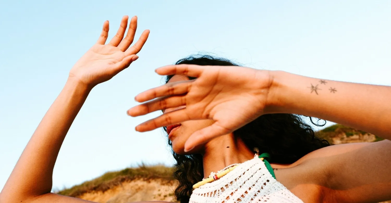 A woman in a white tank top covering her face with her hands
