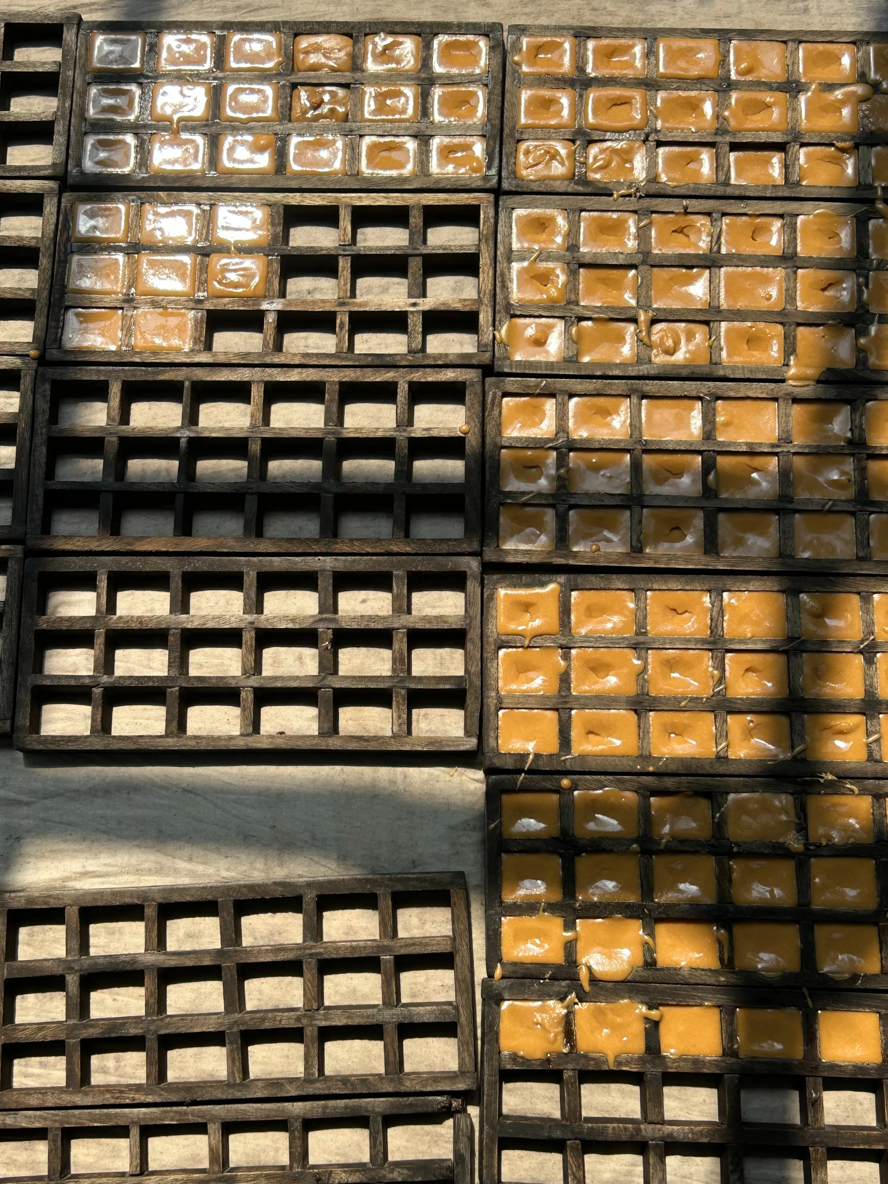 Rows of traditional wooden grid molds filled with thick, golden liquid jaggery (Nolen Gur) as it sets in the sunlight