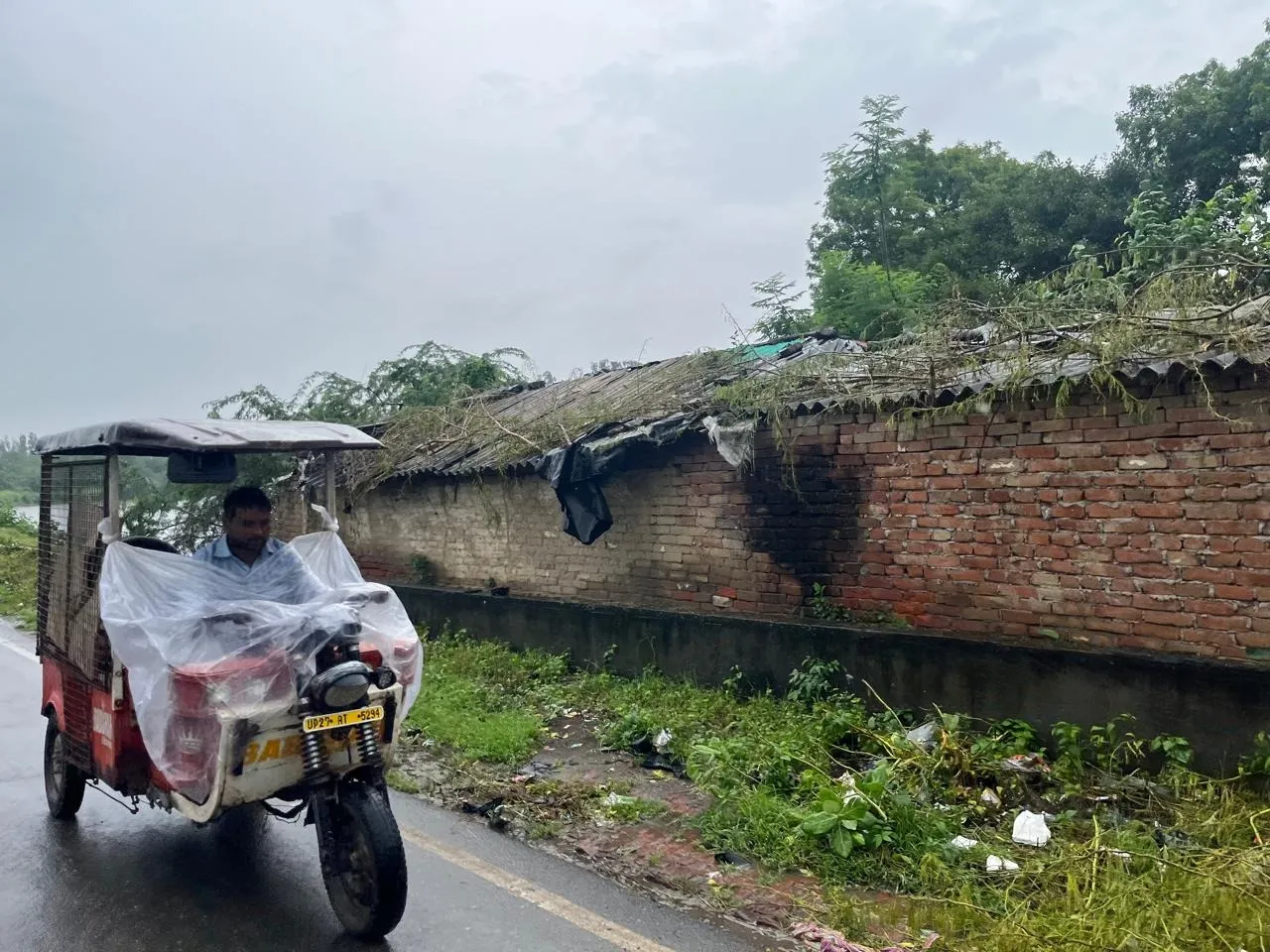 शाहजहांपुर में बारिश से बचाव को ई रिक्शा के सामने बरसाती लगाकर जाता रिक्शाचालक
