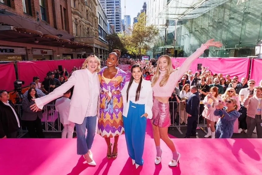 Greta Gerwig, Issa Rae, America Ferrera and Margot Robbie standing on stage smiling with fans behind them