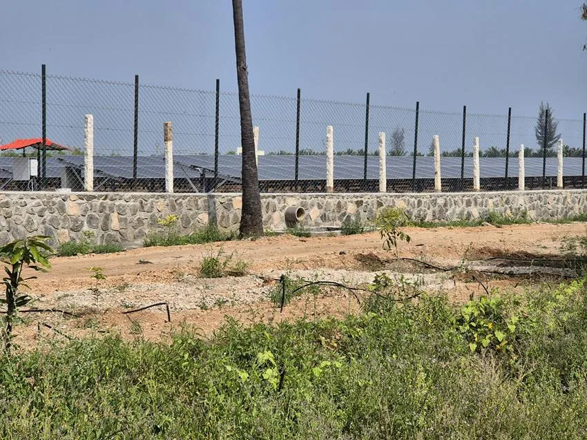 A solar park enclosed by a steel wire fence atop a stone wall with a drainage outlet directing runoff to the surrounding land. Image by Gowthami Subramaniam.
