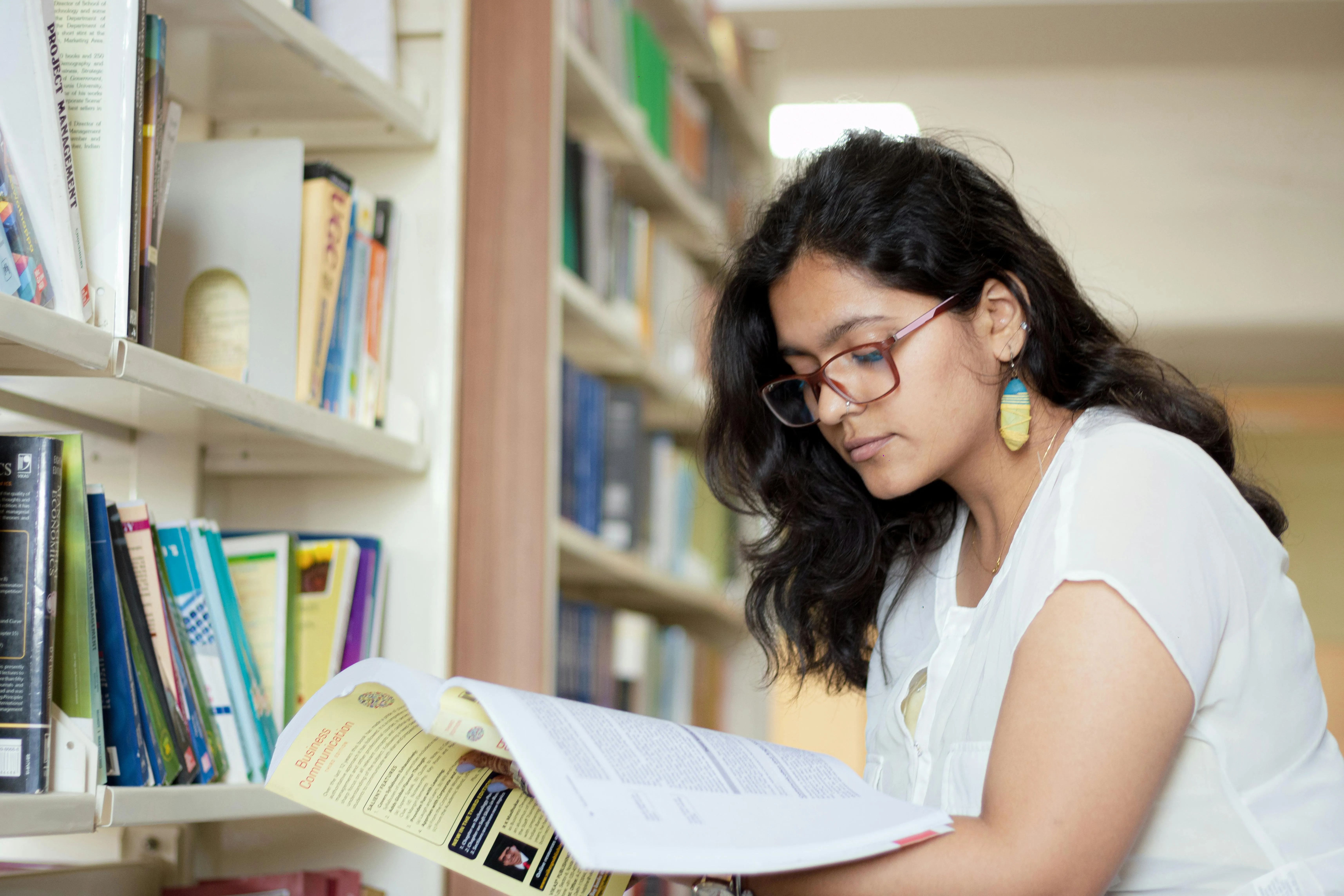 Portrait of a smiling young Indian student reading a book in a library ·  Free Stock Photo