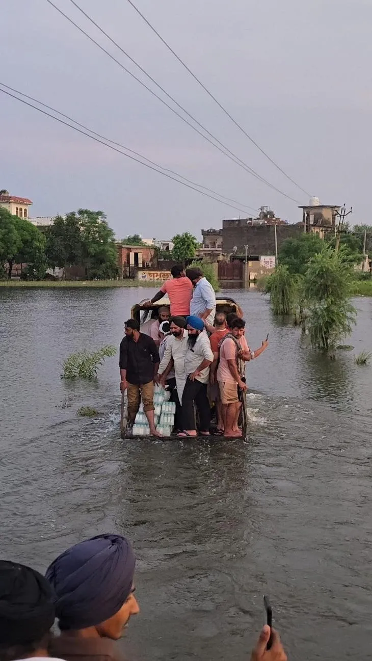 होशियारपुर के डेरा बाबा नानक एरिया के बाढ़ प्रभावित एरिया में पीने वाला पानी और अन्य सामान लेकर जाते हुए लेाग।