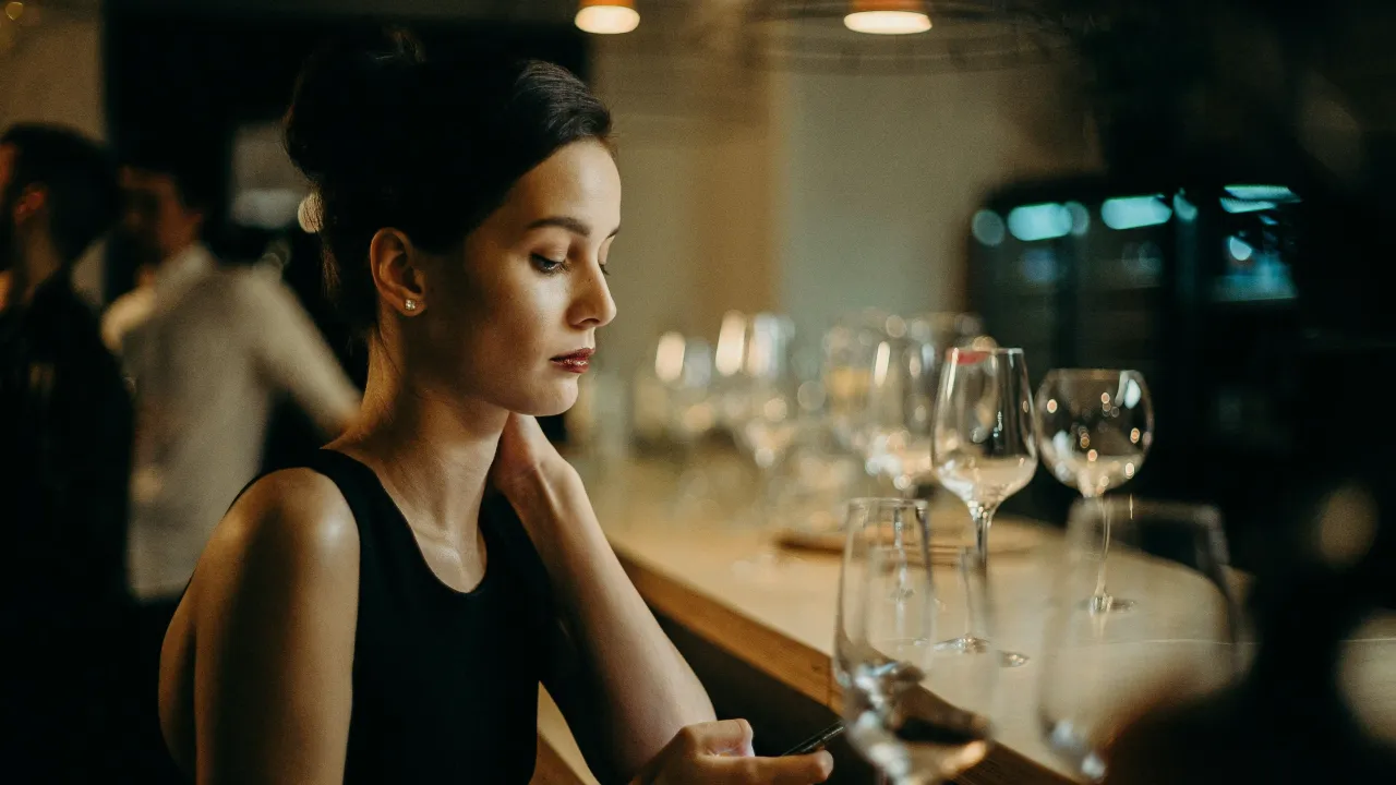 A picture of a woman sitting alone at a bar to show queer loneliness in India, as she browses her phone to show challenges queer people face in dating even when people use dating apps for LGBTQ in India