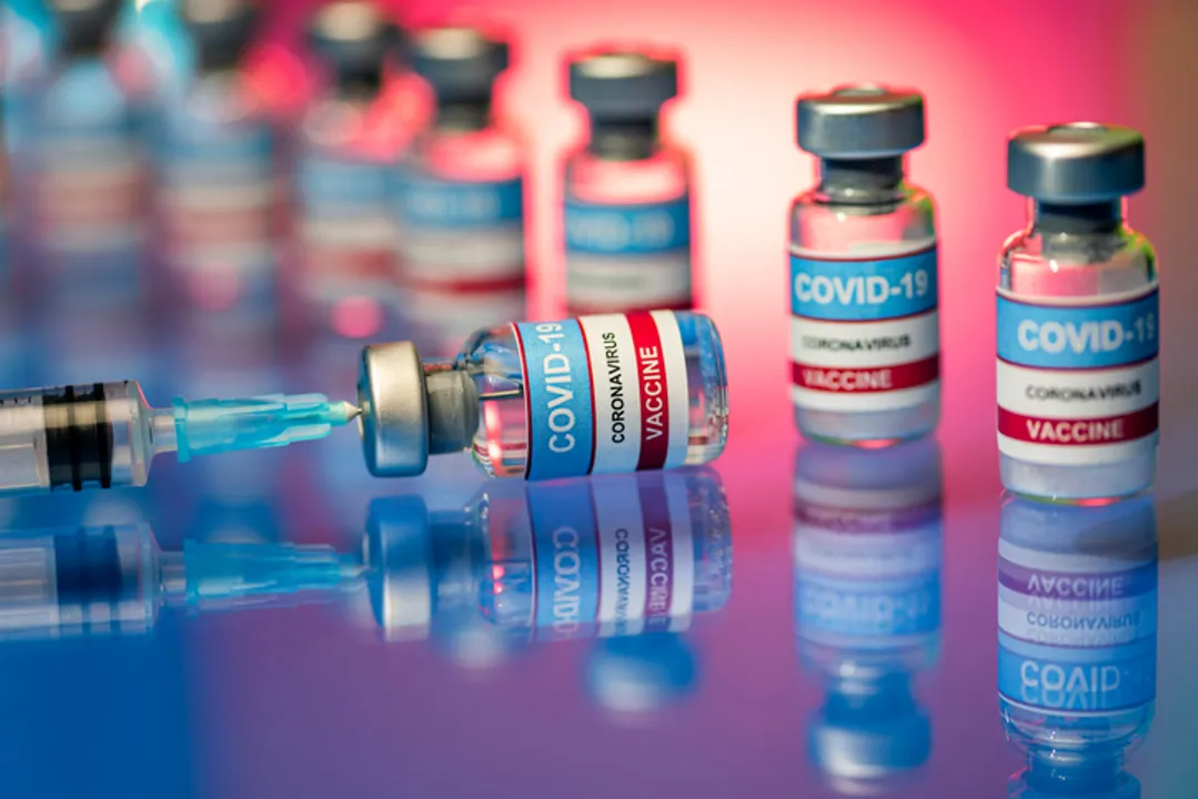  Close up of Covid-19 vaccine - vials and syringe. Glass bottles on a reflective surface 