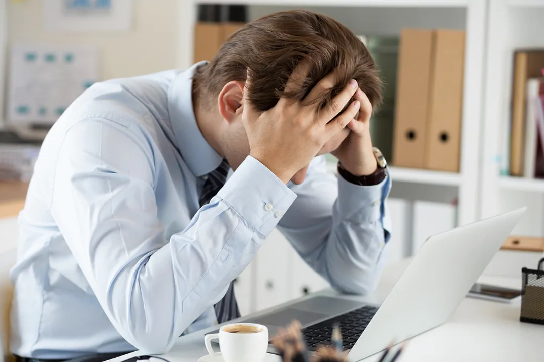  Tired business man at workplace in office holding his head in hands. Sleepy worker early in the morning after late night work. Overworking making mistake stress termination or depression concept 