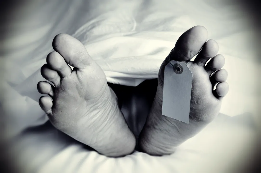  closeup of the feet of a dead body covered with a sheet, with a blank tag tied on the big toe of his left foot, in monochrome, with a vignette added 