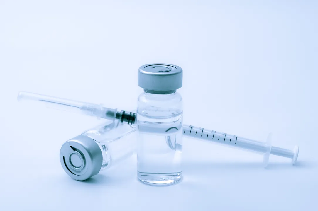  Vaccines, botulinum toxin and insulin ampules concept theme with glass vials with clear liquid next to a syringe and a hypodermic needle isolated on white background 