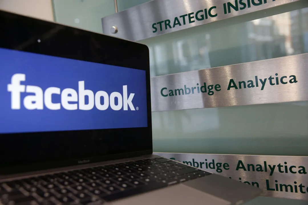  A laptop showing the Facebook logo is held alongside a Cambridge Analytica sign at the entrance to the London offices of Cambridge Analytica. The company's acting CEO, Alexander Tayler, is stepping down, and is the second CEO out since the data sharing scandal broke. 
