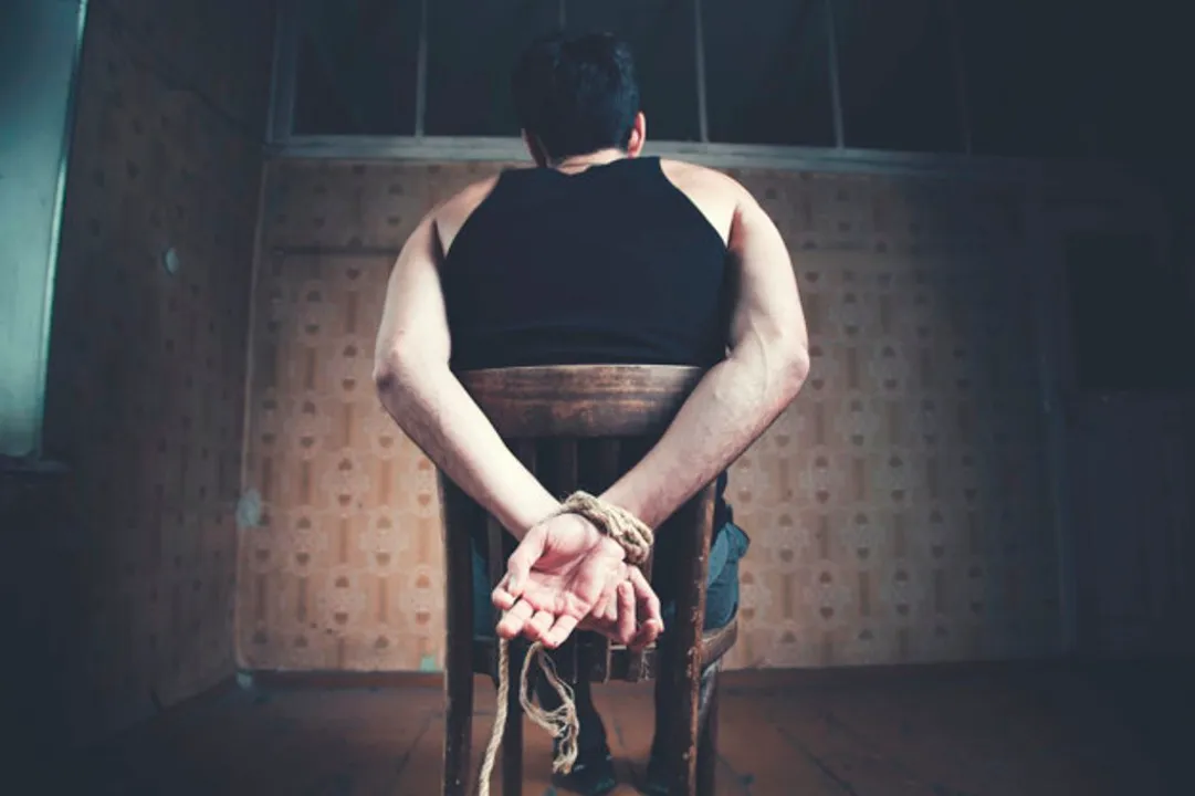  young man tied to chair on dark background 