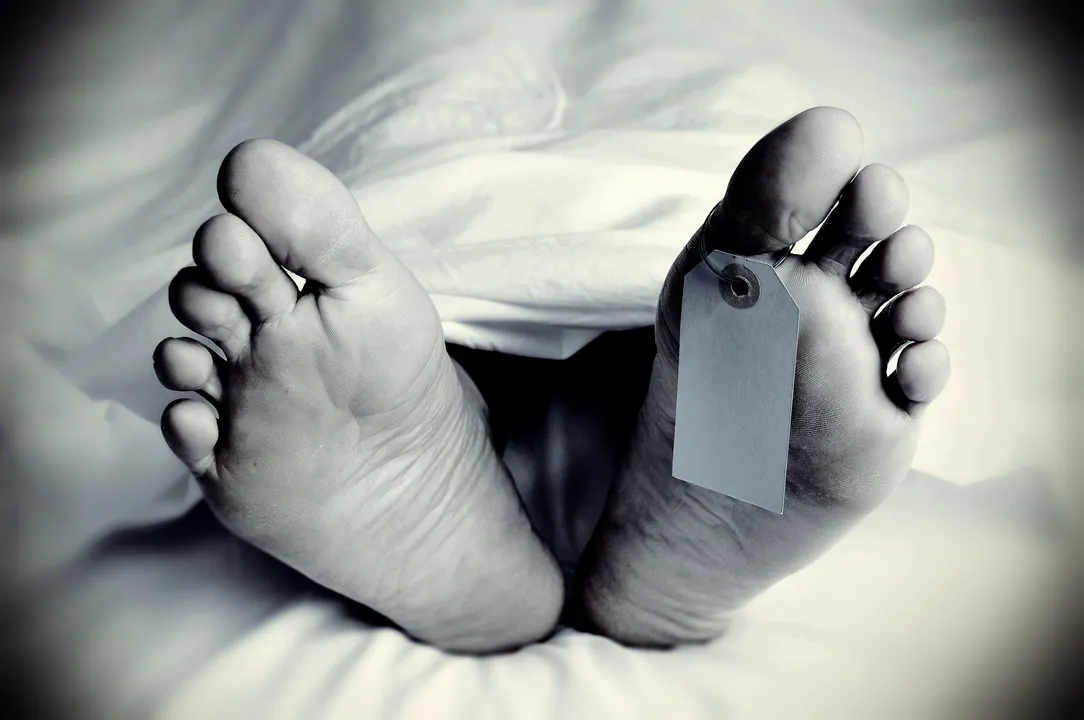  closeup of the feet of a dead body covered with a sheet, with a blank tag tied on the big toe of his left foot, in monochrome, with a vignette added 