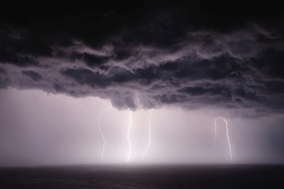  Dark storm clouds with rain and lightning over sea at night. 