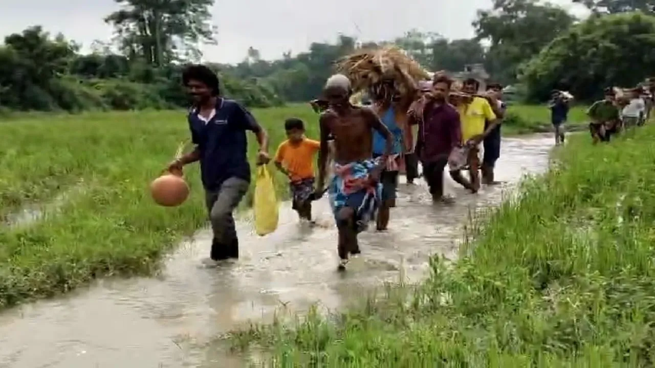 elderly woman body bamboo stretcher mud water,  knee‑deep water mud cremation carried relatives,  West Bengal rural tragic funeral scene  ,flood mud funeral rescue West Bengal,  bamboo bier elderly mud passage,বৃদ্ধার মরদেহ বাঁশের মাচা কাদাজল,  হাঁটু সমান জল কাদা শ্মশানে বহন,  আত্মীয়েরা নদী কাদা পথেই দাফন,  গ্রামীন শ্মশান মৃতদেহ কাদা জল,  বাঁশের মাচায় বৃদ্ধার দেহ কাদা