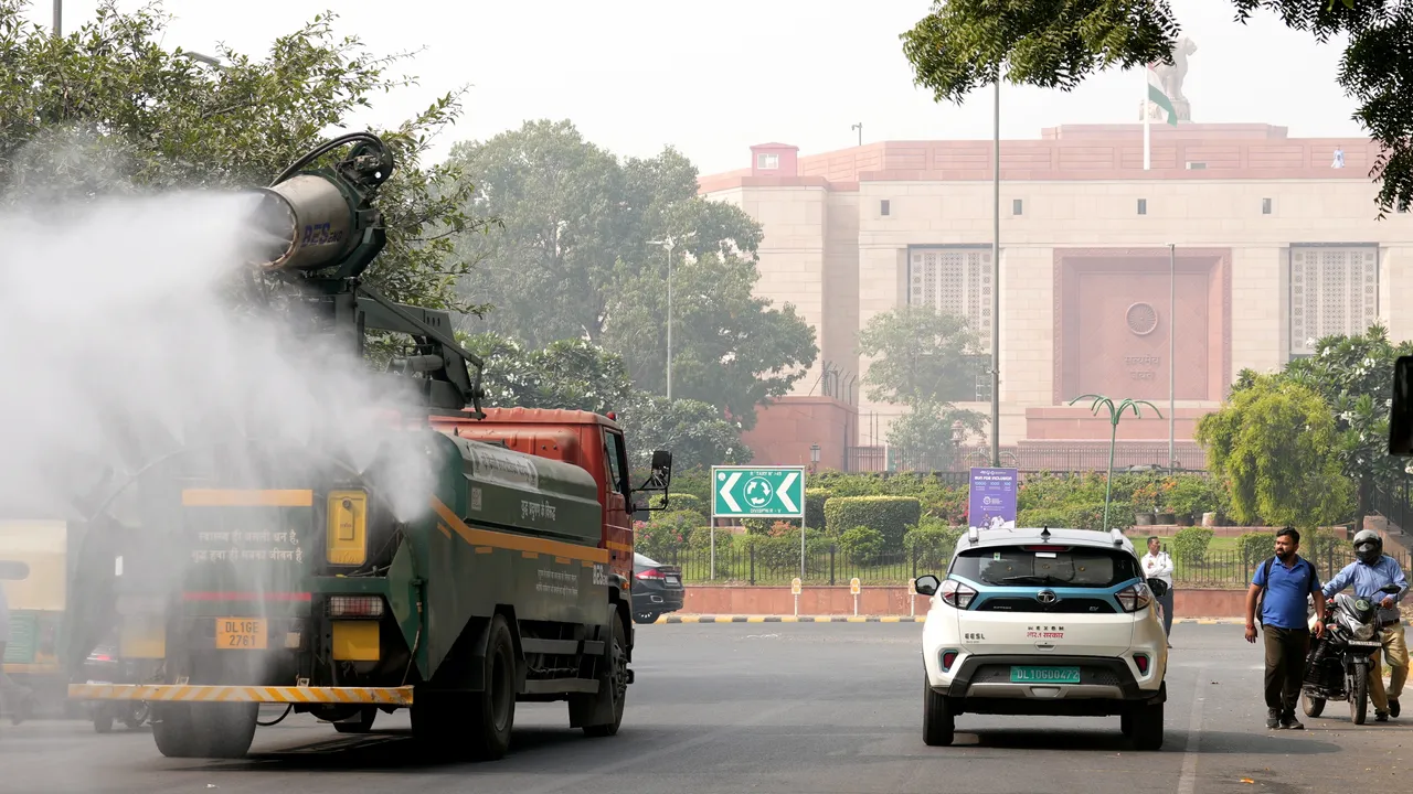 Commuters move past an anti-smog gun spraying water to curb air pollution near the Parliament House, in New Delhi, Saturday, Nov. 9, 2024