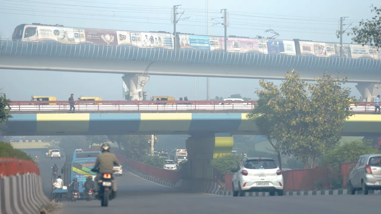 A metro train runs on its track as vehicles ply on a road amid smog, at Dhaula Kuan in New Delhi