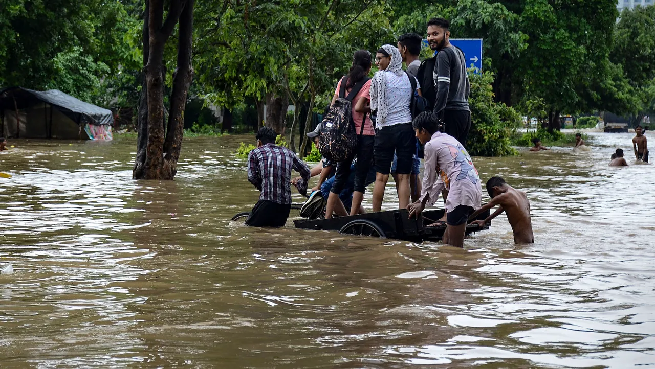 People wade through a waterlogged street after heavy rains, in Gurugram, Sunday, July 9