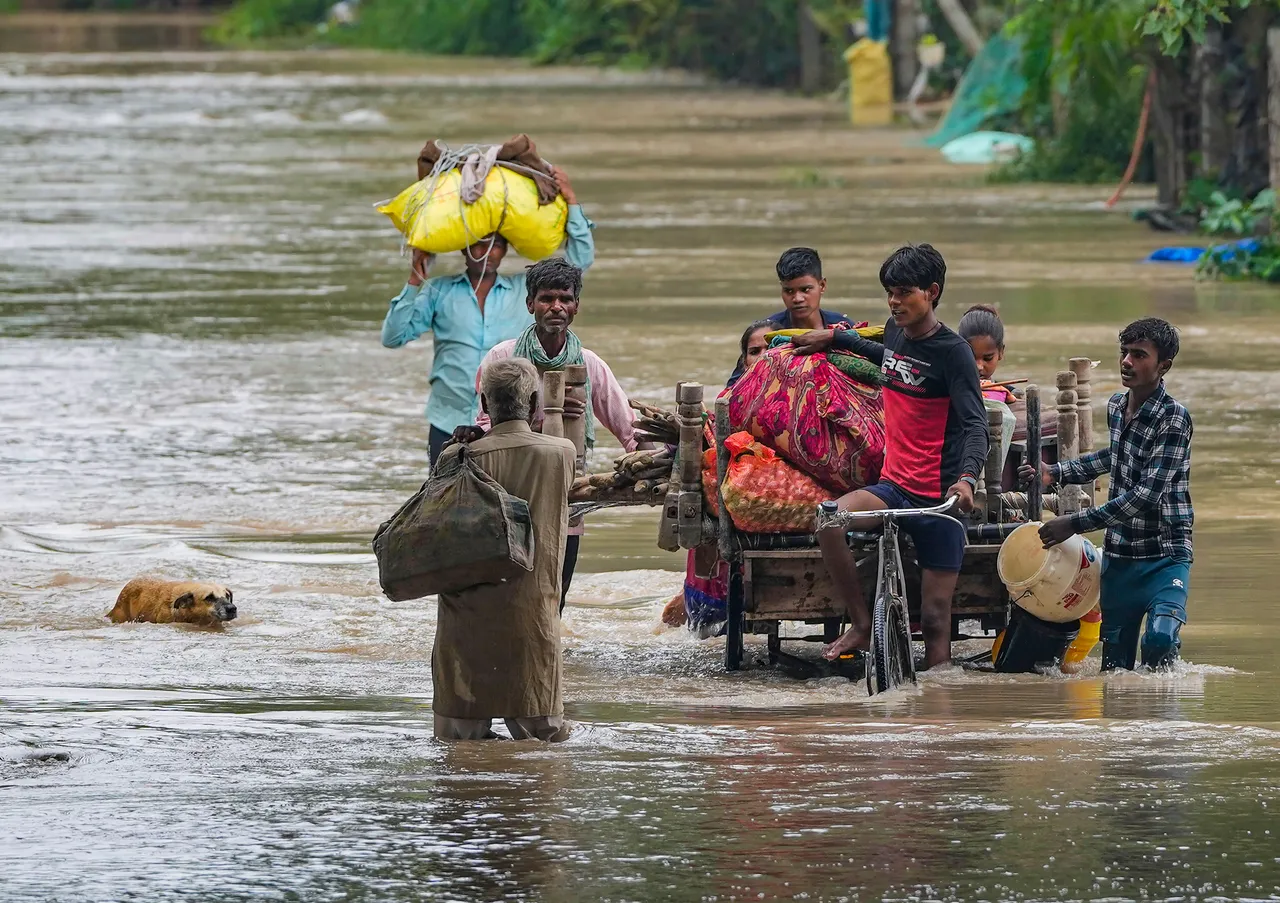 People from low-lying areas around the Yamuna river wade through floodwaters of the swollen river while relocating to a safer place, in New Delhi