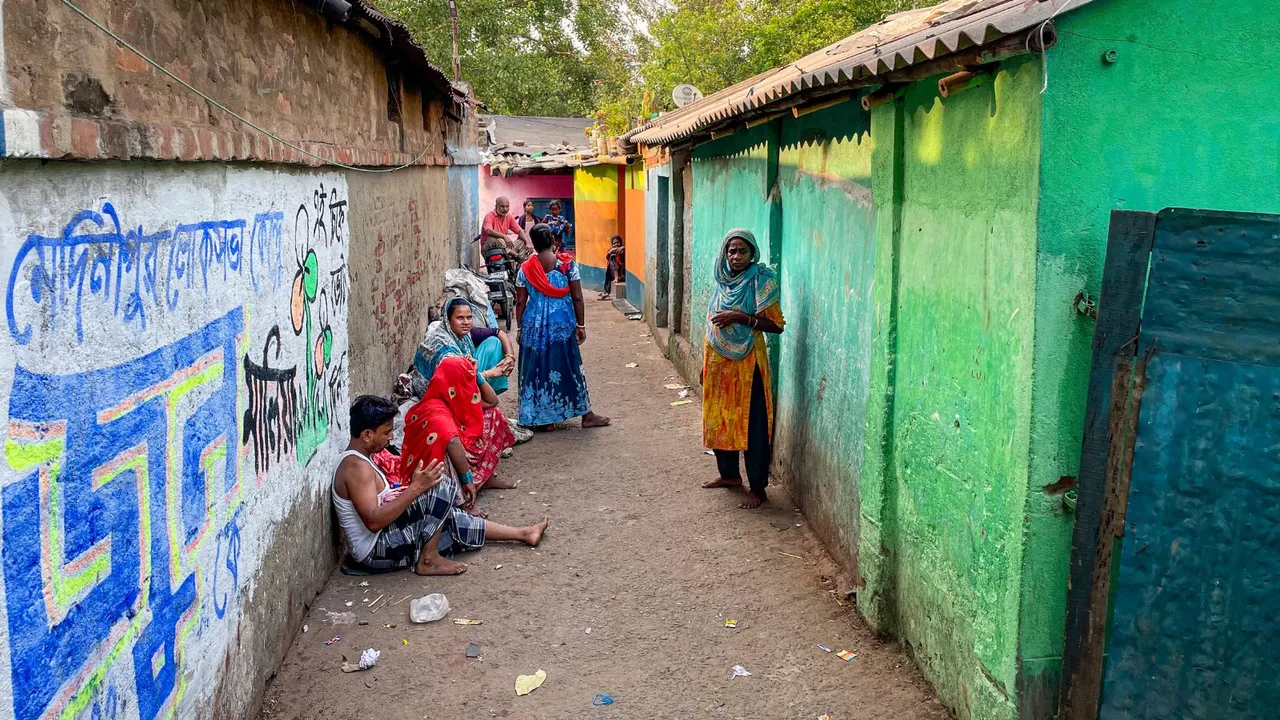 Residents idle at New Bus Stand Gandhi Nagar Bustee in Kharagpur before a wall sporting graffiti for Medinipur's TMC candidate