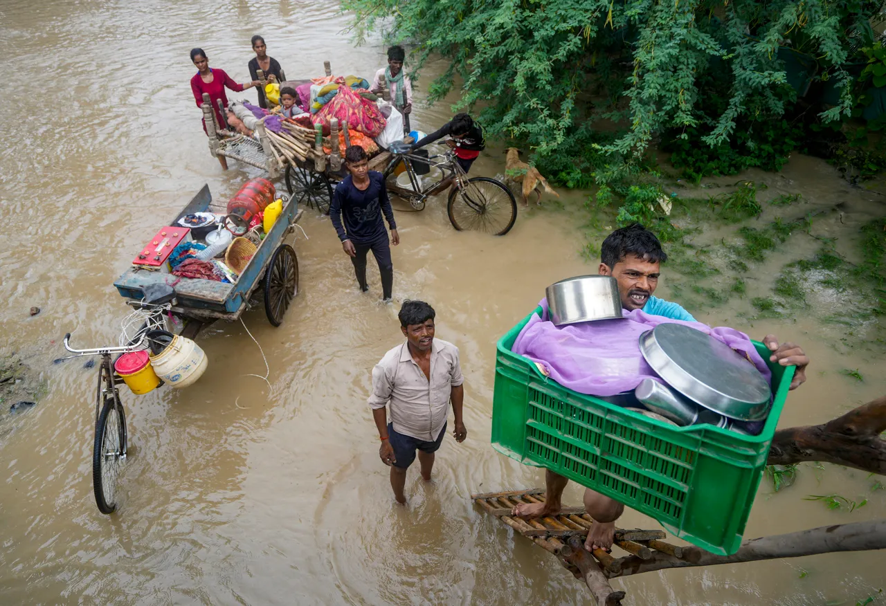People help one another relocate to a safer place after their houses in the low-lying areas around the Yamuna river submerged, in New Delhi