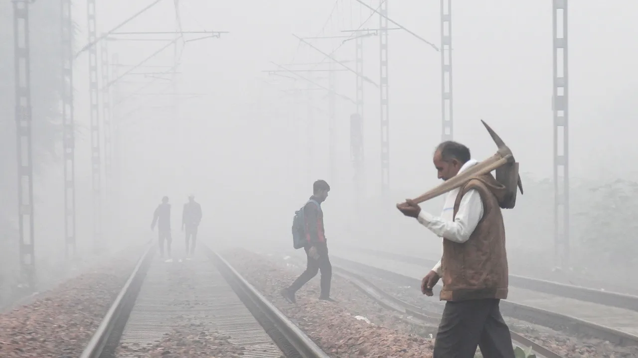 Commuters cross a railway track amid fog on a cold winter morning