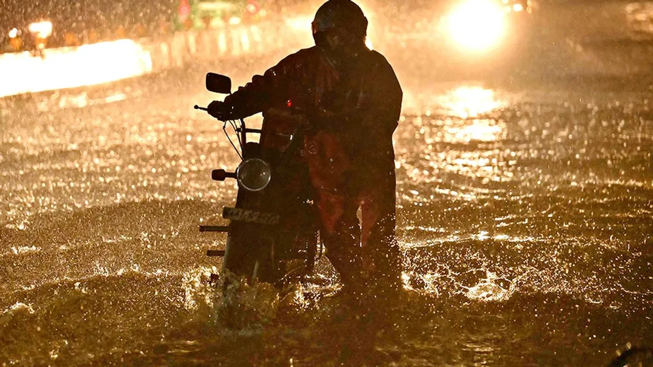A man with his stalled vehicle wades through a waterlogged road during heavy rainfall in Bengaluru on June 2, 2024
