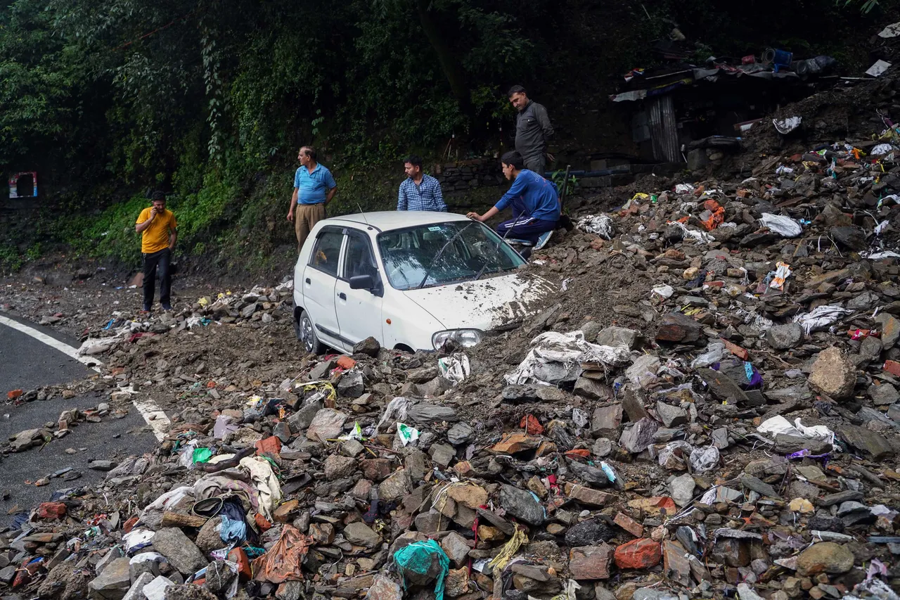 People try to get a vehicle out of debris after it got buried after heavy rainfall, in Shimla