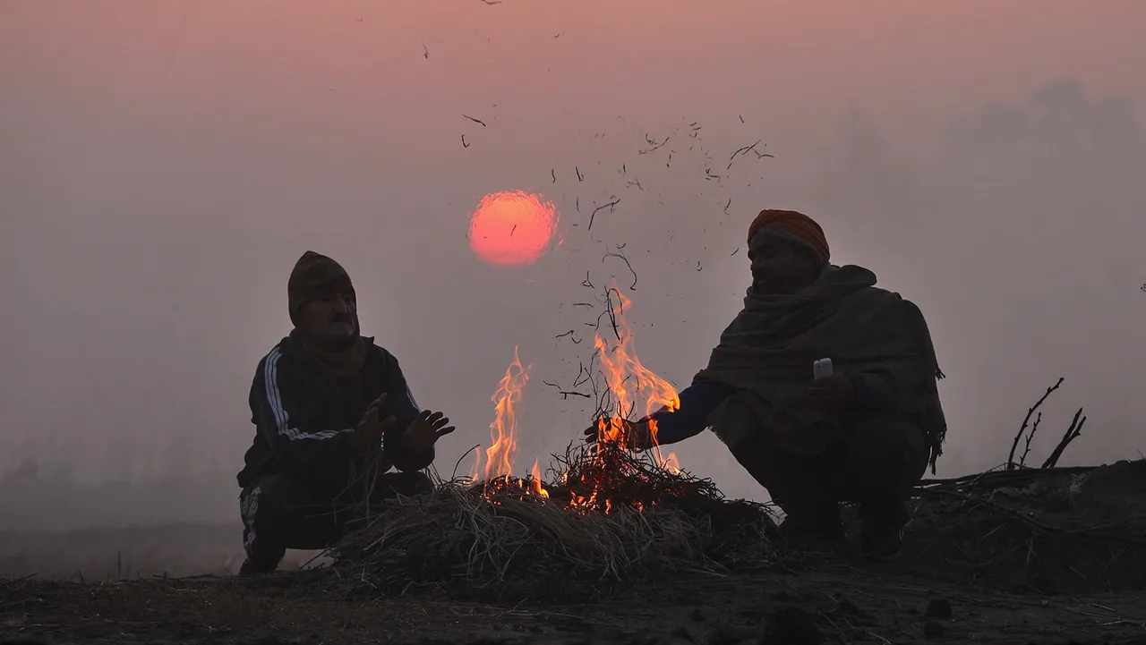 People sit around a bonfire to warm themselves on a cold winter day, in Jammu, early Monday morning