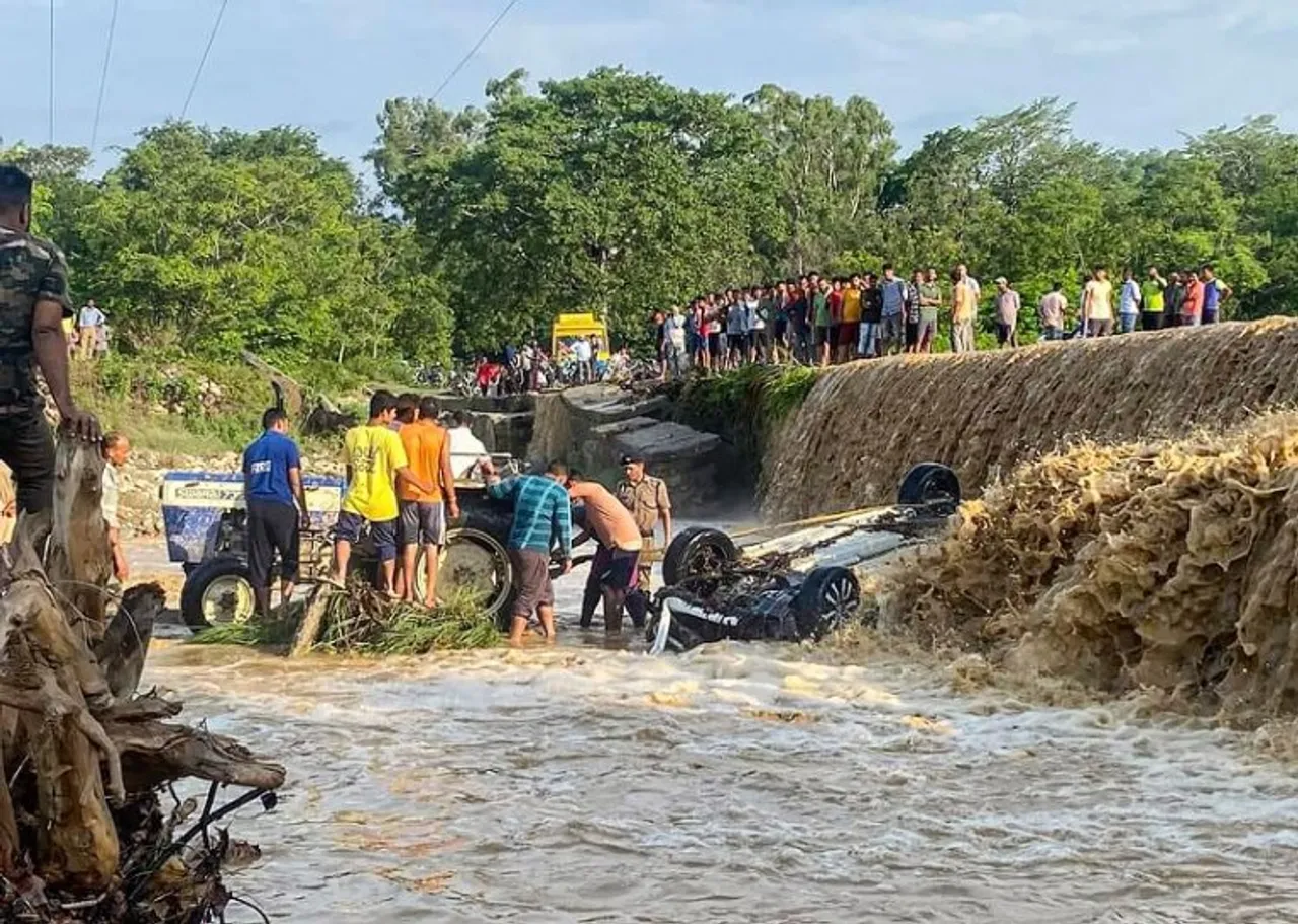 Locals attempt rescue work after a car fell into the Dhela river and was washed away by its strong current, at Ramnagar in Nainital district, Friday