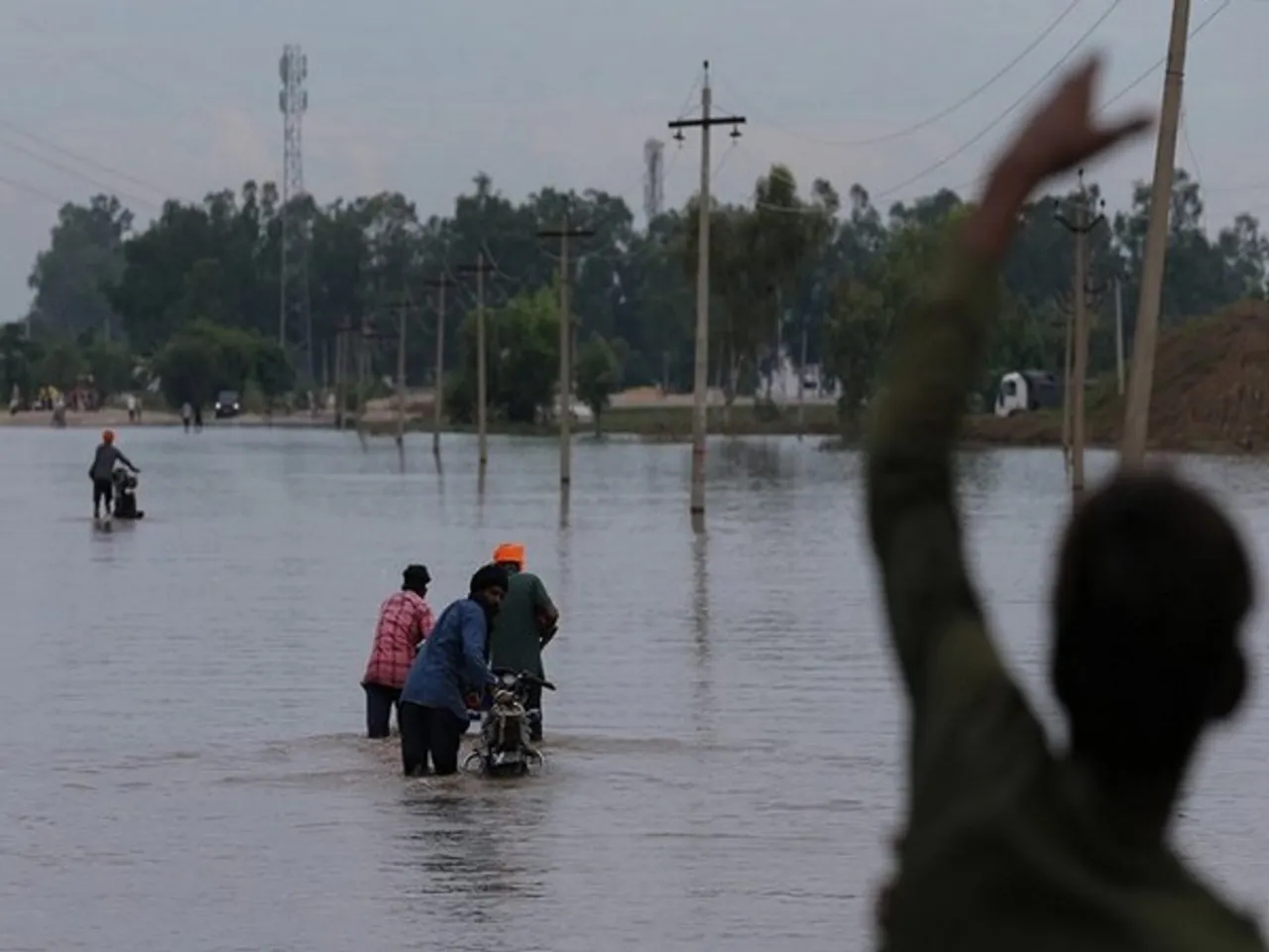 Commuters wade their way through waterlogged roads in the flood-affected area (Photo/ANI)