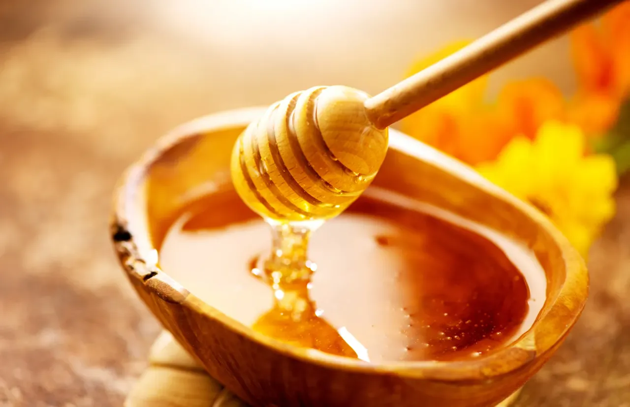 Honey-dripping-from-honey-dipper-in-wooden-bowl