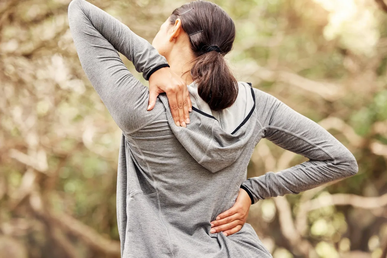 rearview-shot-of-a-woman-experiencing-back-pain-while-working-out-in-nature