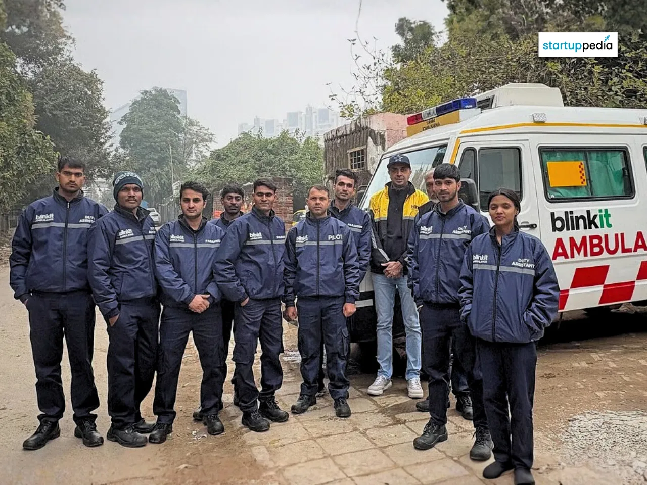A group of Blinkit ambulance staff standing together in uniform beside a Blinkit-branded ambulance outdoors