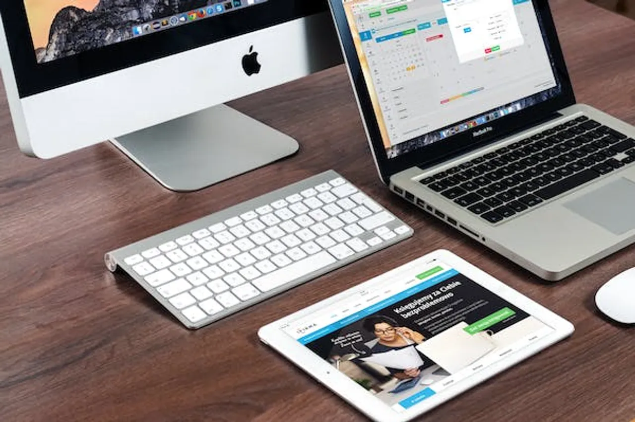 Electronic devices including computer, tablet, and phone neatly arranged on a desk.