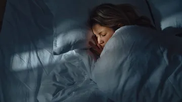 a-white-woman-sleeping-peacefully-in-bed-in-a-darkened-room-with-a-soft-light-falling-across-her-face-16X9-1024x576