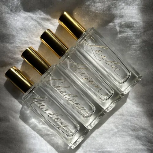 This may contain: four empty perfume bottles sitting next to each other on a white sheet with gold caps