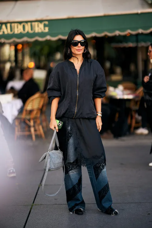 stylish individual wearing a black zipup top and layered denim pants