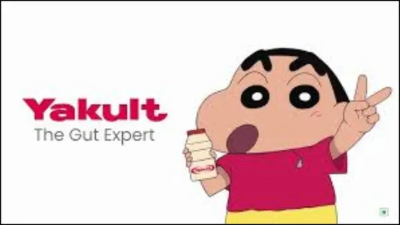 The animated character Shin Chan is shown with a bottle of Yakult, smiling and holding a pose that suggests energy and health. The background is bright and kid-friendly.