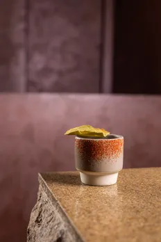 A drink with a red spicy rim and a yellow garnish