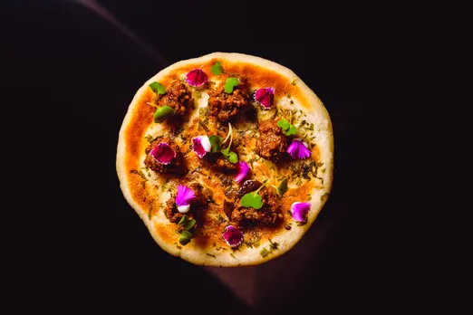A picture of an India flatbread with pieces of chicken and leaves and flowers as topping
