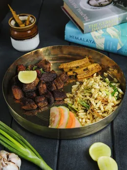 A small plate with meat pieces, some salad, pickle, and puffed rice