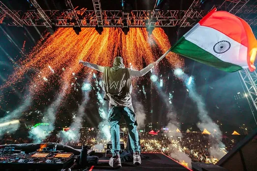 A picture of Alan Walker performing in India, waving the national flag of India as a means to show the rise of the electronic music in India as well as the evolution of DJs in India