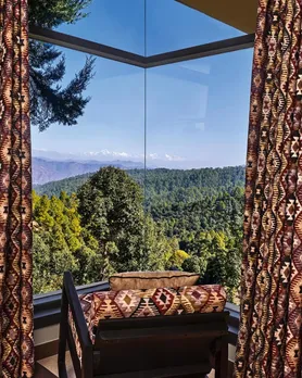 A picture of a cosy chair at the corner of a room with a view of a mountain  range to show how luxury boutique hotels in India can be enjoyed in the monsoon.